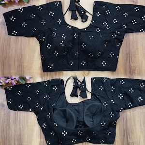 Puede incluir: Una blusa negra bordada con mangas cortas y cuello redondo. La blusa está decorada con pequeñas lentejuelas plateadas en un patrón geométrico.