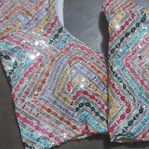 Puede incluir: Un top de tela blanca con un patr&oacute;n geom&eacute;trico colorido hecho de lentejuelas. El top tiene un escote en V y es sin mangas.