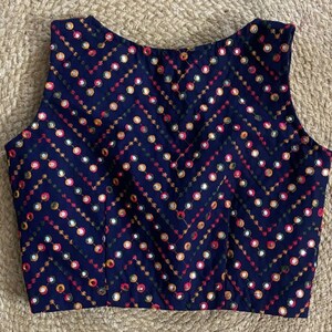 Puede incluir: Una blusa azul marino sin mangas con un patr&oacute;n de chevron y bordado de espejo de colores.