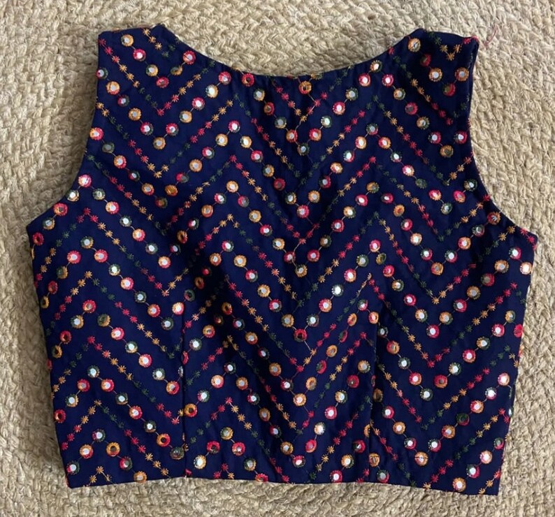 Puede incluir: Una blusa azul marino sin mangas con un patr&oacute;n de chevron y bordado de espejo de colores.