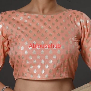 Może przedstawiać: Blusa w kolorze brzoskwiniowym z srebrnym wzorem liści i dekoltem łódkowym. Bluzka jest krótka i ma krótkie rękawy. Tekst "Ablousehub" jest widoczny z przodu bluzki.