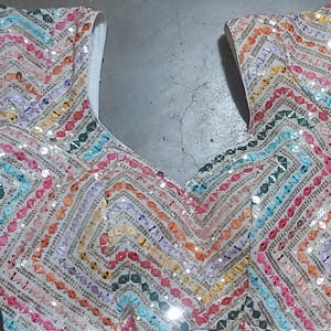 Puede incluir: Un top de tela blanca con un patr&oacute;n de chevron colorido hecho de lentejuelas. Las lentejuelas son en tonos de rosa, naranja, amarillo, verde, azul y morado.