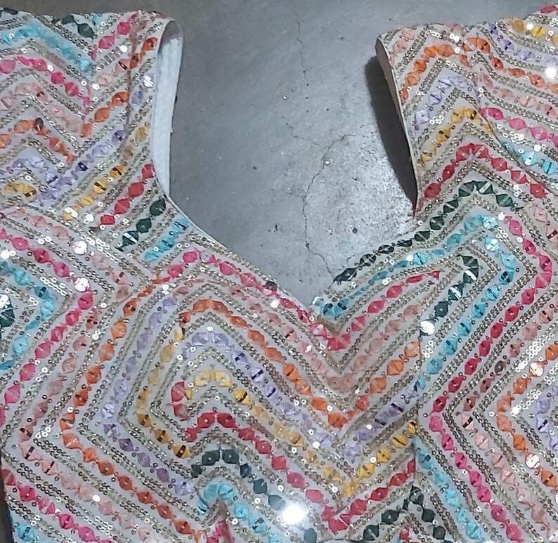 Puede incluir: Un top de tela blanca con un patr&oacute;n de chevron colorido hecho de lentejuelas. Las lentejuelas son en tonos de rosa, naranja, amarillo, verde, azul y morado.