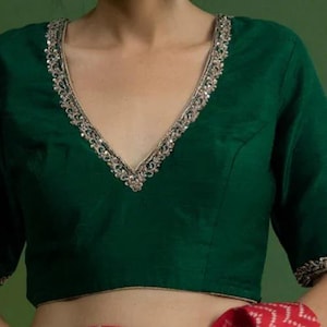 May include: A deep green sleeveless blouse with a V-neckline and silver embellishments around the neckline and sleeves.