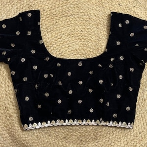 Puede incluir: Una blusa de terciopelo negro con cuello redondo y mangas cortas. La blusa está decorada con pequeños puntos blancos bordados y un ribete blanco alrededor del cuello y las mangas.