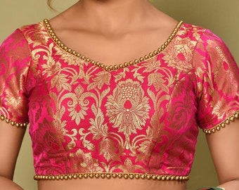 Puede incluir: Una blusa de brocado rosa con bordados dorados y un escote con cuentas. La blusa tiene mangas cortas y un corpiño ajustado.