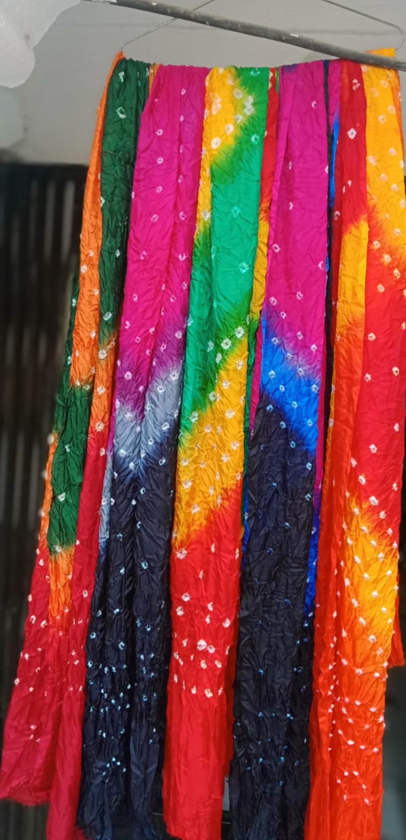 May include: A collection of colorful tie-dye scarves hanging on a clothesline. The scarves are made of a soft, flowing fabric and feature a variety of vibrant colors, including orange, red, green, blue, and purple. The scarves are decorated with a white tie-dye pattern.
