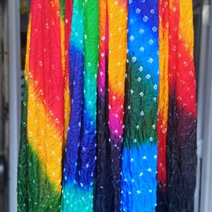 May include: A collection of eight colorful tie-dye scarves with white polka dots. The scarves are arranged in a row and are hanging from a metal rod.