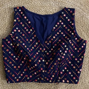 Puede incluir: Una blusa azul marino sin mangas con escote en V y un patr&oacute;n geom&eacute;trico de espejos bordados de colores.