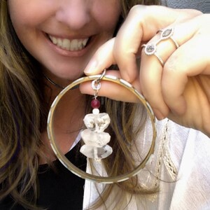 May include: A gold bangle bracelet with a clear crystal charm hanging from it. The charm is made of several stacked clear crystals with a small red bead at the top.