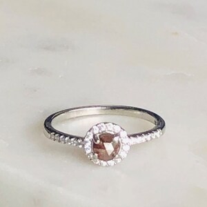 May include: A silver ring with a round, brown diamond surrounded by a halo of smaller diamonds.