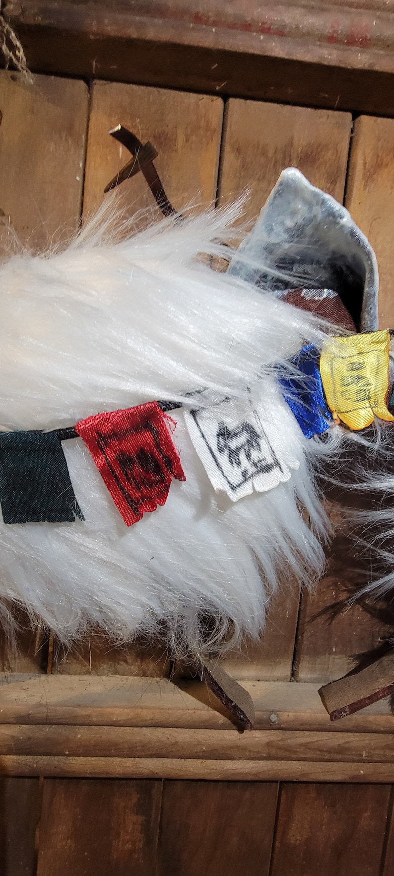 K&ouml;nnte beinhalten: Wei&szlig;es, flauschiges Garn mit einer Schnur aus bunten Stoffgebetfahnen. Die Fahnen sind gr&uuml;n, rot, wei&szlig;, blau und gelb. Die Fahnen haben verschiedene Symbole und Designs.
