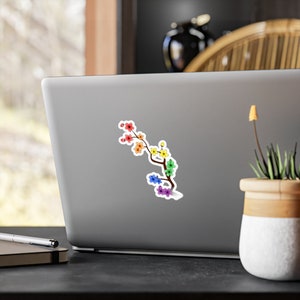 Pu&ograve; includere: Un ramo di ciliegio in fiore dai colori dell'arcobaleno con uno stelo marrone e foglie verdi. I fiori sono disposti a forma di arcobaleno, iniziando dal rosso in alto e terminando con il viola in basso.