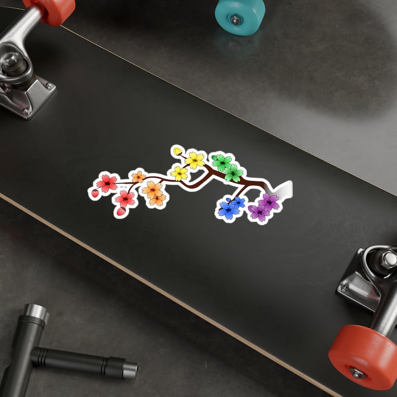 Pu&ograve; includere: Un ramo di ciliegio in fiore arcobaleno con uno stelo marrone e foglie verdi. I fiori sono disposti in fila, con i colori che passano dal rosso all'arancione, al giallo, al verde, al blu, all'indaco e al viola.