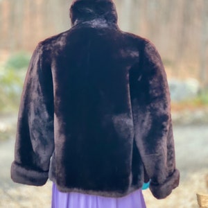 May include: A brown faux fur jacket with a high collar and long sleeves. The jacket is on a mannequin and the background is blurred.