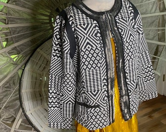 May include: Black and white geometric patterned jacket with a gold trim. The jacket has a round neckline and a front zip closure.