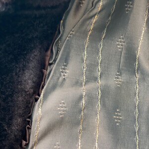 May include: Close-up of a dark brown fabric with a green fabric lining. The lining has a repeating diamond pattern and thin gold stripes.