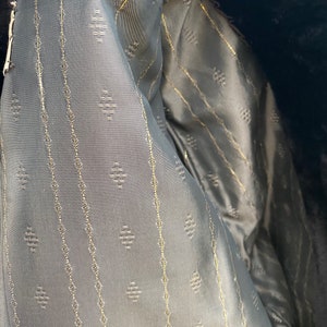 May include: Close-up of the lining of a garment, showing a dark gray fabric with a subtle diamond pattern and thin gold lines.