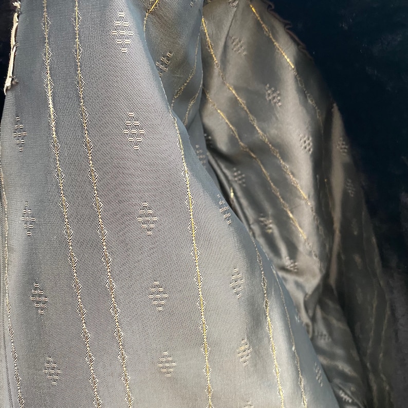 May include: Close-up of the lining of a garment, showing a dark gray fabric with a subtle diamond pattern and thin gold lines.