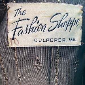 May include: A white label with black text that reads "The Fashion Shoppe Culpeper, VA". The label has a handwritten number "10" on the left side.