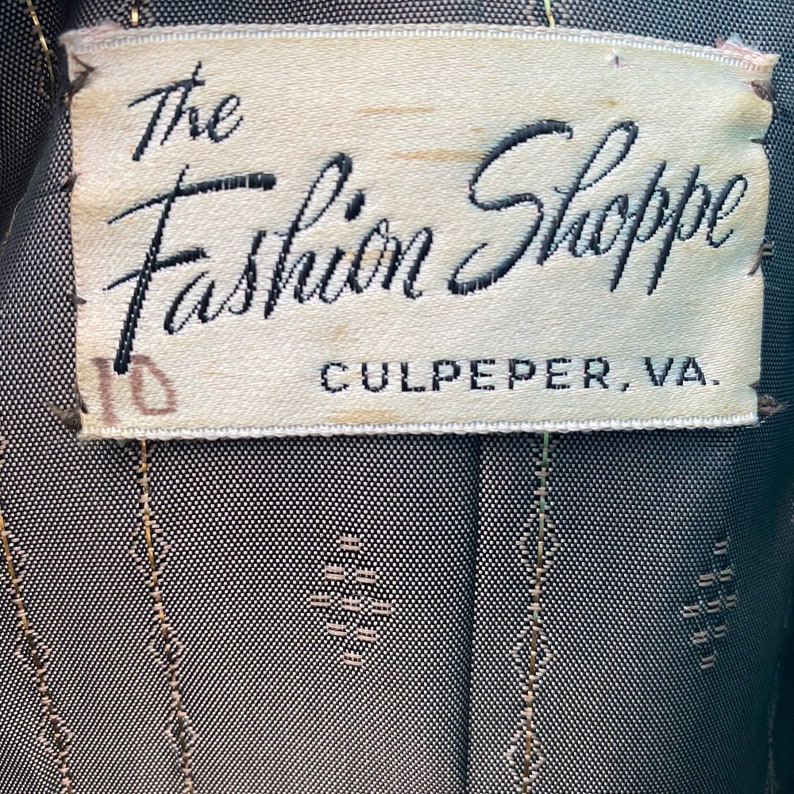 May include: A white label with black text that reads "The Fashion Shoppe Culpeper, VA". The label has a handwritten number "10" on the left side.