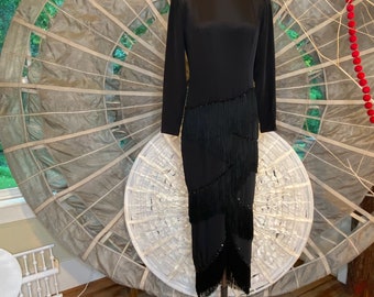 May include: A black long-sleeved dress with a mock neck and a fringe hem. The dress is adorned with black beads.