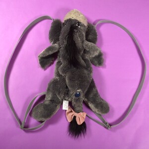 May include: Gray plush donkey backpack with a pink bow and adjustable straps.