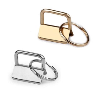Könnte beinhalten: Zwei Schlüsselringe, einer in Gold und einer in Silber, mit einer quadratischen Schlaufe und einem runden Ring.
