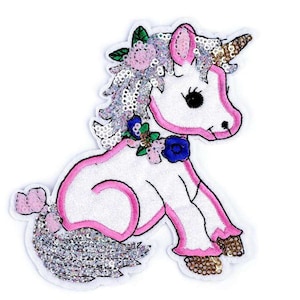 Könnte beinhalten: Ein weißes Einhorn mit rosa Akzenten und einem silbernen Pailletten-Schwanz. Das Einhorn trägt eine Blumenkrone und ein goldenes Horn.