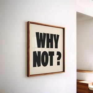 Peut inclure: Un cadre avec l'inscription "WHY NOT?" en lettres noires et grasses. L'impression a un fond crème et est encadrée dans un cadre en bois. L'œuvre est accrochée sur un mur blanc.