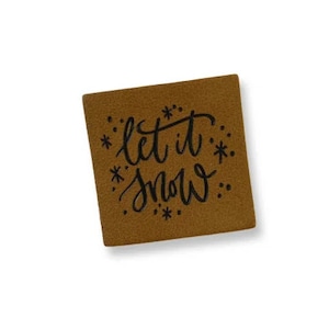 May include: A brown felt square with the text "Let it snow" in black cursive lettering surrounded by small black stars.