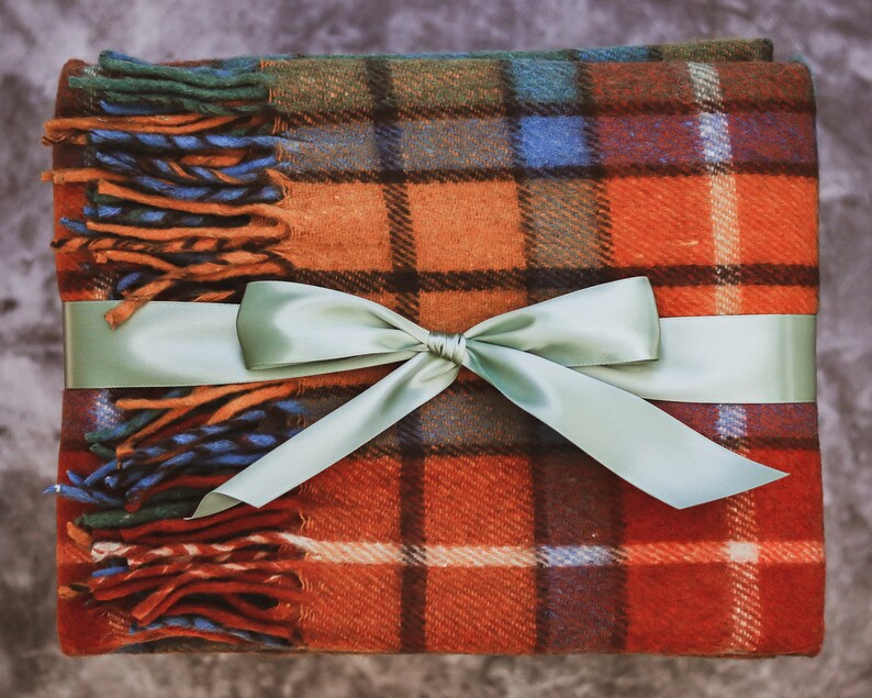 May include: A red, orange, green, and blue plaid throw blanket with a sage green satin ribbon tied in a bow.