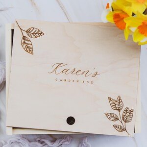 May include: A wooden box with a light wood finish and a brown engraved design of leaves and the text "Karen's Garden Box".
