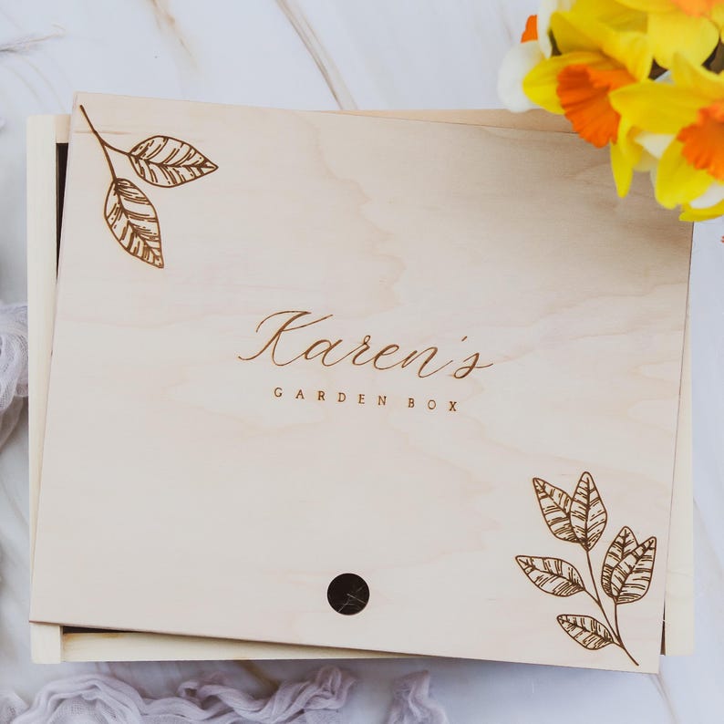 May include: A wooden box with a light wood finish and a brown engraved design of leaves and the text "Karen's Garden Box".