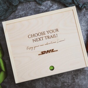 May include: A wooden box with the text "Choose your next trail!" and "Enjoy your new adventures Luann!" engraved on the lid. The DHL logo is also engraved on the lid.