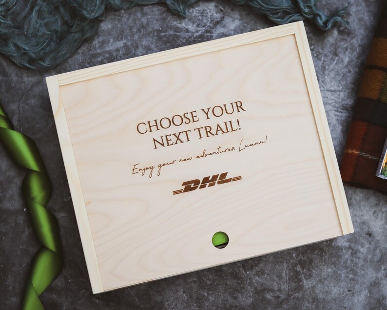 May include: A wooden box with the text "Choose your next trail!" and "Enjoy your new adventures Luann!" engraved on the lid. The DHL logo is also engraved on the lid.
