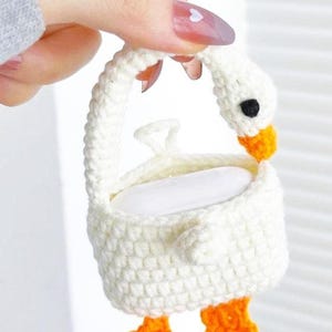 以下が含まれることがあります： オレンジ色の足が付いた白の編み物でできた白鳥の形をした石鹸置き。石鹸置きには持ち手があり、白い石鹸が入っています。