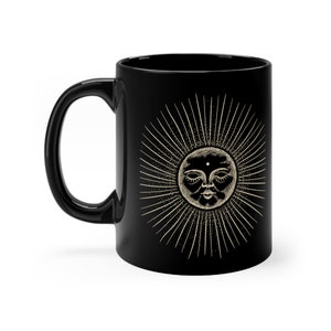 May include: Black ceramic mug with a white sun illustration. The sun has a face with closed eyes and a small dot on its forehead. The sun is surrounded by rays.
