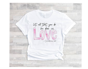 May include: White t-shirt with a pink and white watercolor design that says "Let all that you do be done in LOVE" with the scripture reference "1 Corinthians 16:14" underneath.