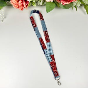 Op de afbeelding: Een patchwork lanyard met rode paisley-, marineblauwe en lichtblauwe gingham patronen. Het heeft een zilverkleurige metalen sluiting. De stof is verticaal gerangschikt.