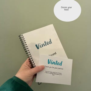May include: A hand holding a white spiral-bound notebook, a translucent sheet, and a white card. The notebook and card have the word "Vinted" in teal. The card reads "Thank you for your purchase". A white circle with "Choose your items" is in the background.