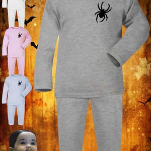 May include: A gray long-sleeved pajama set with a black spider graphic on the chest. Additional pajama sets in white, pink, and light blue are also shown. The background has a Halloween theme.
