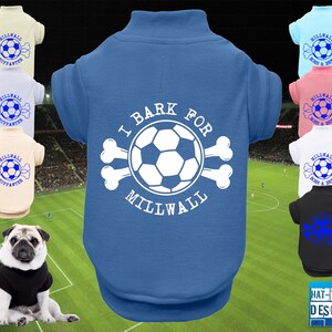 Peut inclure: Plusieurs t-shirts pour chiens de différentes couleurs, dont le bleu, le rose, le blanc et le noir. Chaque chemise présente un motif de ballon de football avec le texte "I Bark For Millwall" ou "Millwall Born & Bred". Un carlin porte une chemise noire.