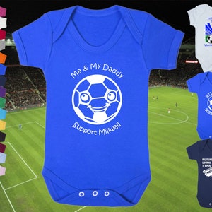 May include: A blue baby onesie with a white soccer ball design. The soccer ball has a smiling face and the text "Me & My Daddy Support Millwall".