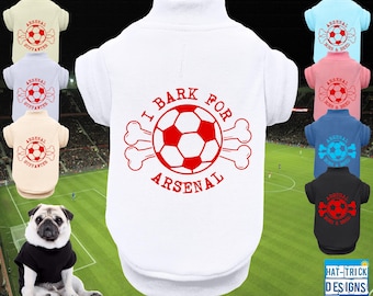 May include: Dog apparel in various colors, including white, black, blue, and pink, with soccer-themed designs. The white shirt features a red soccer ball and the text "I BARK FOR ARSENAL." Other shirts display the Arsenal logo.