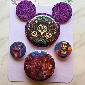 May include: A set of purple glittery Mickey Mouse ear-shaped embellishments and five round Coco-themed buttons. The buttons feature colorful illustrations of characters and scenes from the animated movie, including skulls and guitars.
