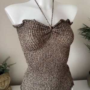 May include: A brown and metallic gold crochet halter top featuring a textured, open-knit pattern, a ruffled neckline, and a thin braided neck strap that secures at the centre front with a small, round, metallic bead detail.