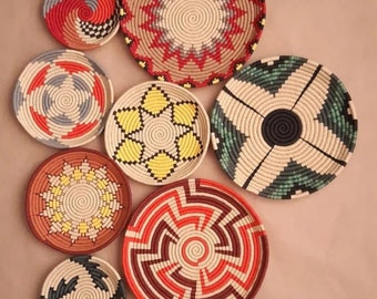 May include: A set of eight woven wall baskets with various geometric patterns in red, yellow, green, black, and white.