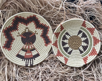 May include: Two round woven baskets with intricate geometric patterns. One basket has brown, red, and white stripes, while the other has green, brown, and white stripes.