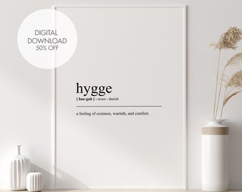 Könnte beinhalten: Ein schwarz-weißer druckbarer Wandkunstdruck mit dem Wort "hygge", definiert als ein Gefühl von Gemütlichkeit, Wärme und Komfort. Der Druck ist gerahmt und auf einem Regal mit einer Vase getrockneter Pampasgräser ausgestellt.